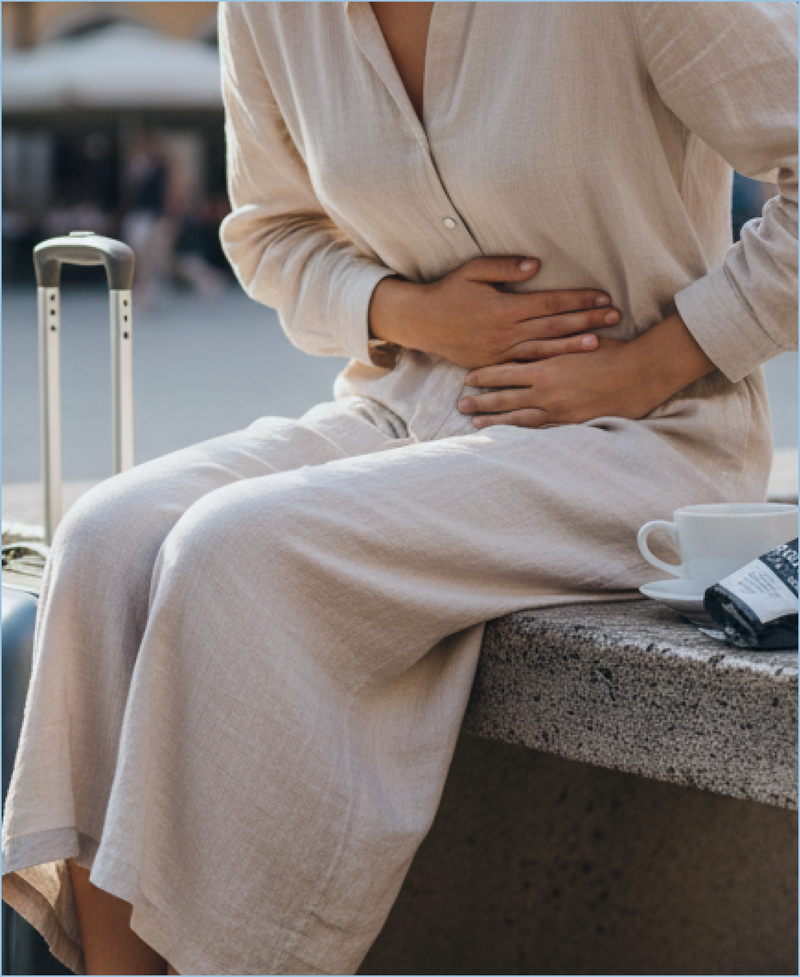 Traveler holding stomach while seated with suitcase